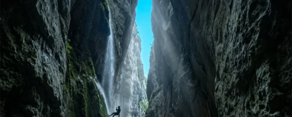 Vue en contre-plongée d'une gorge étroite du Vercors avec parois calcaires vertigineuses, cascade et canyoneur en rappel au premier plan illustrant l'échelle monumentale.
