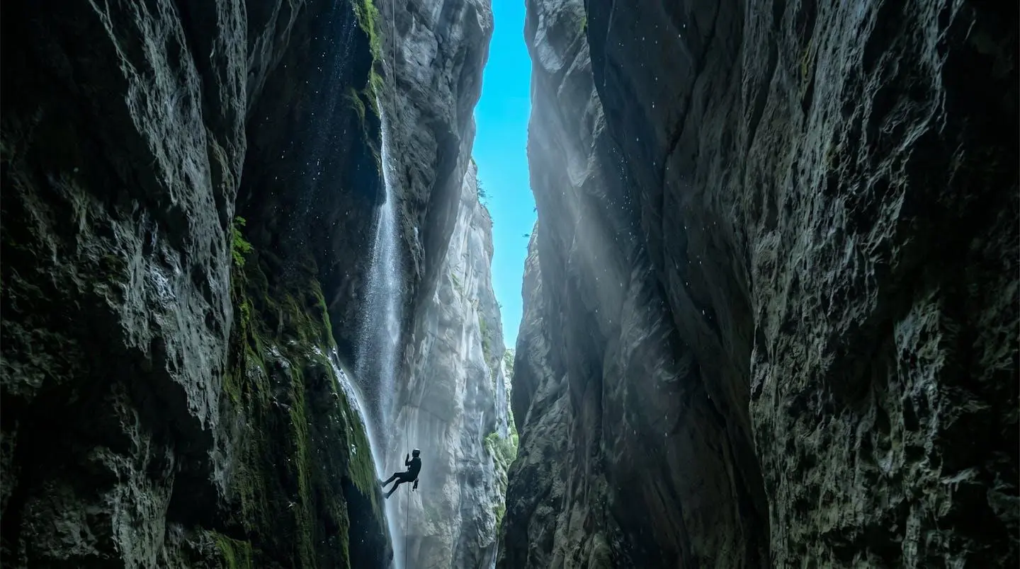 Vue en contre-plongée d'une gorge étroite du Vercors avec parois calcaires vertigineuses, cascade et canyoneur en rappel au premier plan illustrant l'échelle monumentale.